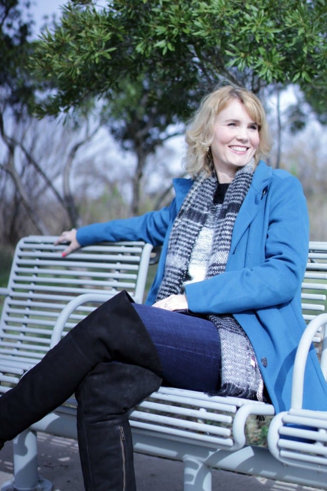 Women's winter coat in blue, paired with over the knee boots.