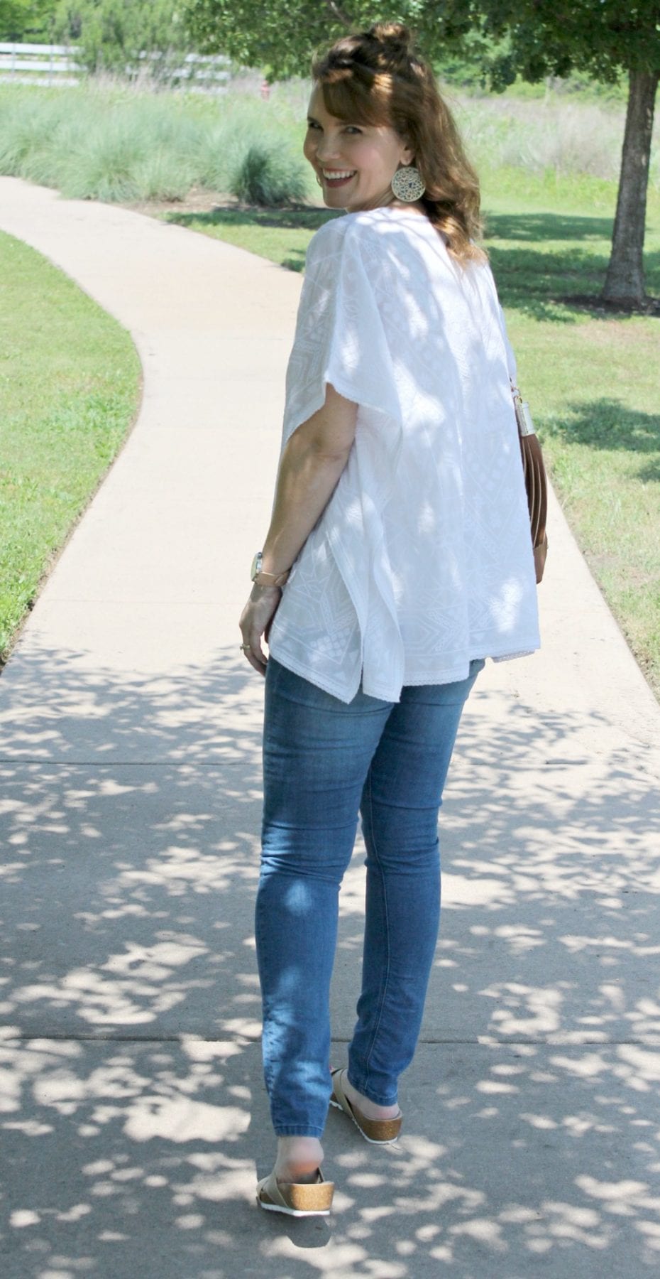 Casual spring outfit idea - White embroidered poncho, light denim, gold sandals from Secret Celebrity and a brown tassel handbag.