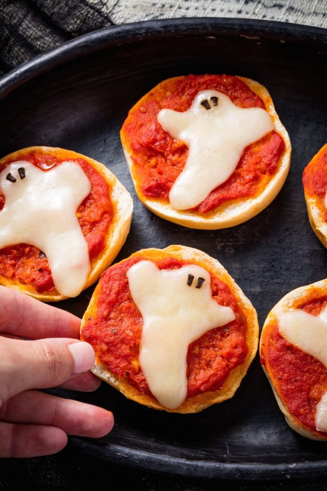 A bagel topped with tomato sauce and mozzarella cheese in the shape of a ghost.