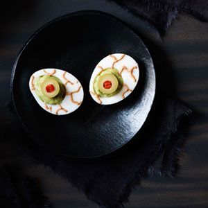 Hard boiled eggs with a pile of guacamole in place of the yolk, with an olive in the middle to look like a pupil, and red lines on the side to mimic a bloodshot eyeball.